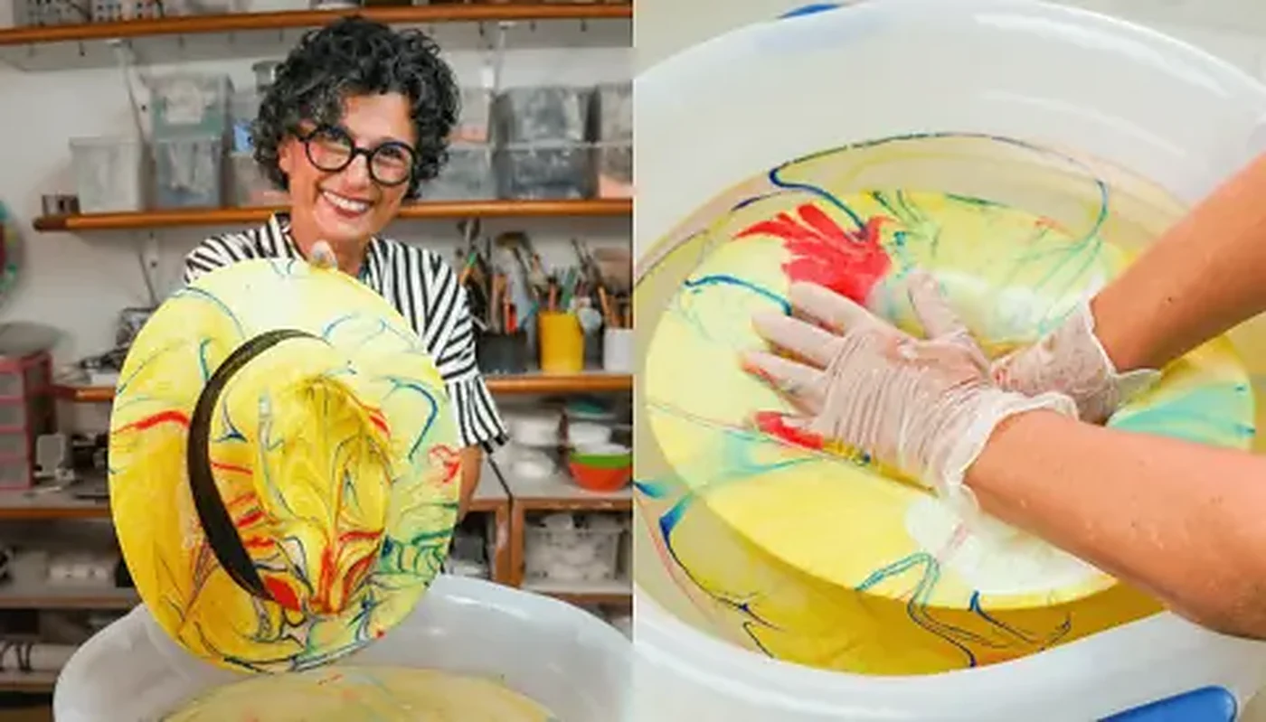 Lúcia Eid mostra um chapéu de tecido marmorizado em cores vivas, ao lado da bacia de tinta